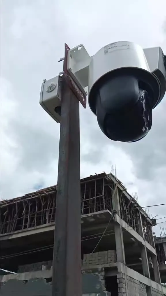 Hikvision PTZ dome camera on a steel pole with a junction box, next to a building under construction